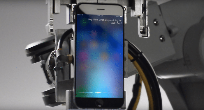 Borítókép: Liam, a robot egy ártatlanul várakozó iPhone-t tart a robotkarjában, amin Siri kérdezi tőle, hogy mivel tölti a Föld napját.