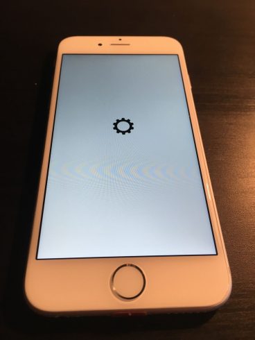 Kép: Az iPhone 6 prototípus szoftverének betöltődési képernyője, egy fekete fogaskerék van a fehér képernyő közepén az alma logó helyett.
