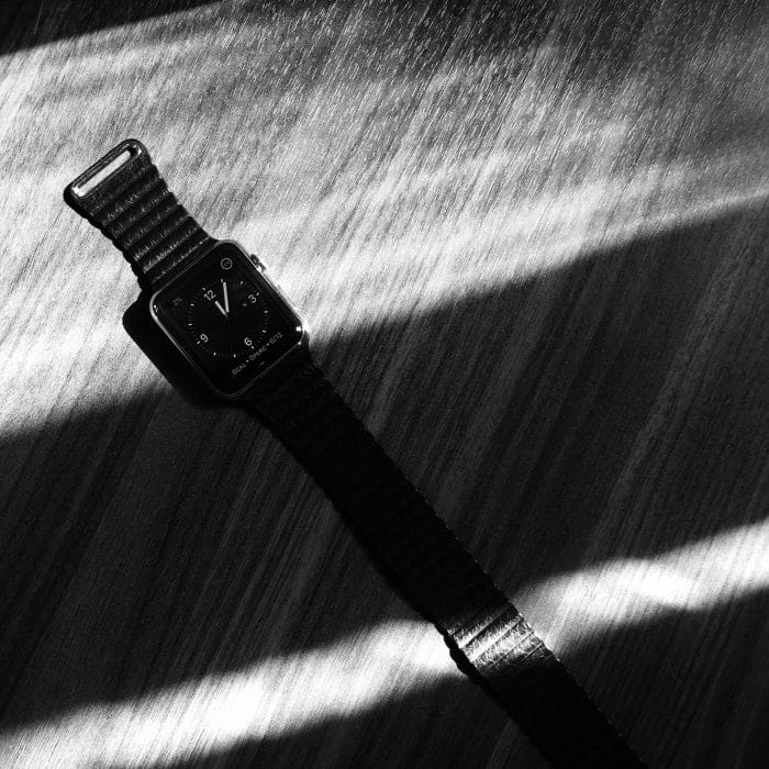 Fekete leather loop szíj egy asztroszürke órával egy fekete-fehér képen, fény és árnyék csíkok között.