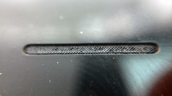 Makró fotó – egy iPhone 7 hangszórórácsa, amin a rácsozat nyílásaiban látható az abba lerakódott, a nyílásokat eltömő szennyeződés