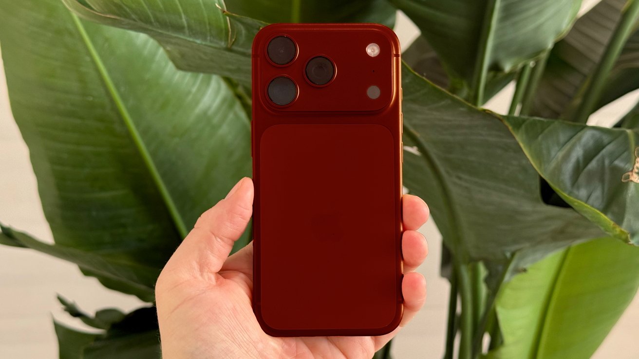 Kézben tartott sötétpiros iPhone 18 Pro látványterve nagy zöld trópusi levelek előtt, lágy, természetes fényben.