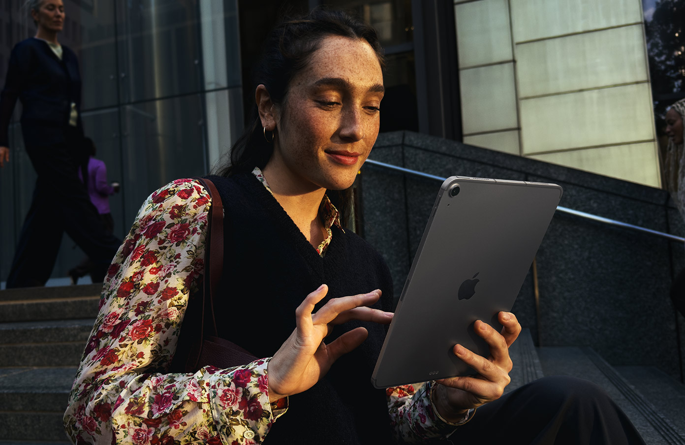 Valaki egy nagy épület előtti lépcsőn ülve asztroszürke 11 hüvelykes iPad Airt használ, zökkenőmentes Wi‑Fi-kapcsolattal a hálózaton keresztüli adatátvitelhez.